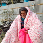 Elderly man smiles and wraps his new, thick, pink blanket around his shoulders.