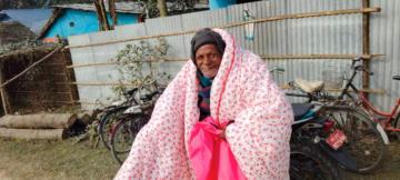 Elderly man smiles and wraps his new, thick, pink blanket around his shoulders.